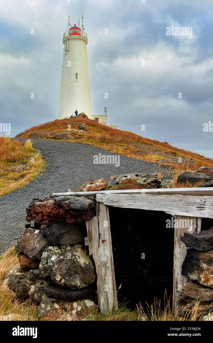 Phare de Reykjanesta. Au sommet d'une colline avec un ciel nuageux en arrière-plan. Le phare est entouré de rochers et d'une structure en bois Banque D'Images