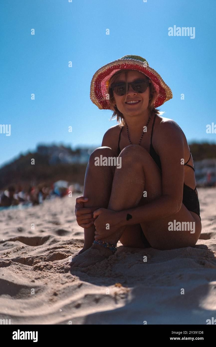 Une femme en maillot de bain et un chapeau multicolore repose sur la plage. Banque D'Images