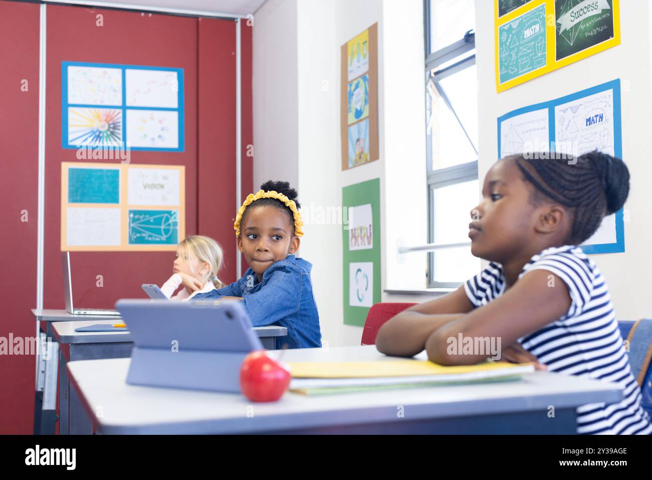 À l'école, les filles multiraciales utilisant des tablettes et des ordinateurs portables tout en étant assis à un bureau Banque D'Images