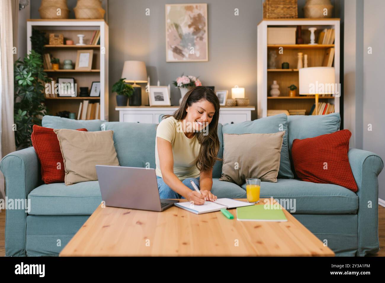 Femme souriante multitâche à la maison, écrivant des notes lors d'une réunion virtuelle Banque D'Images