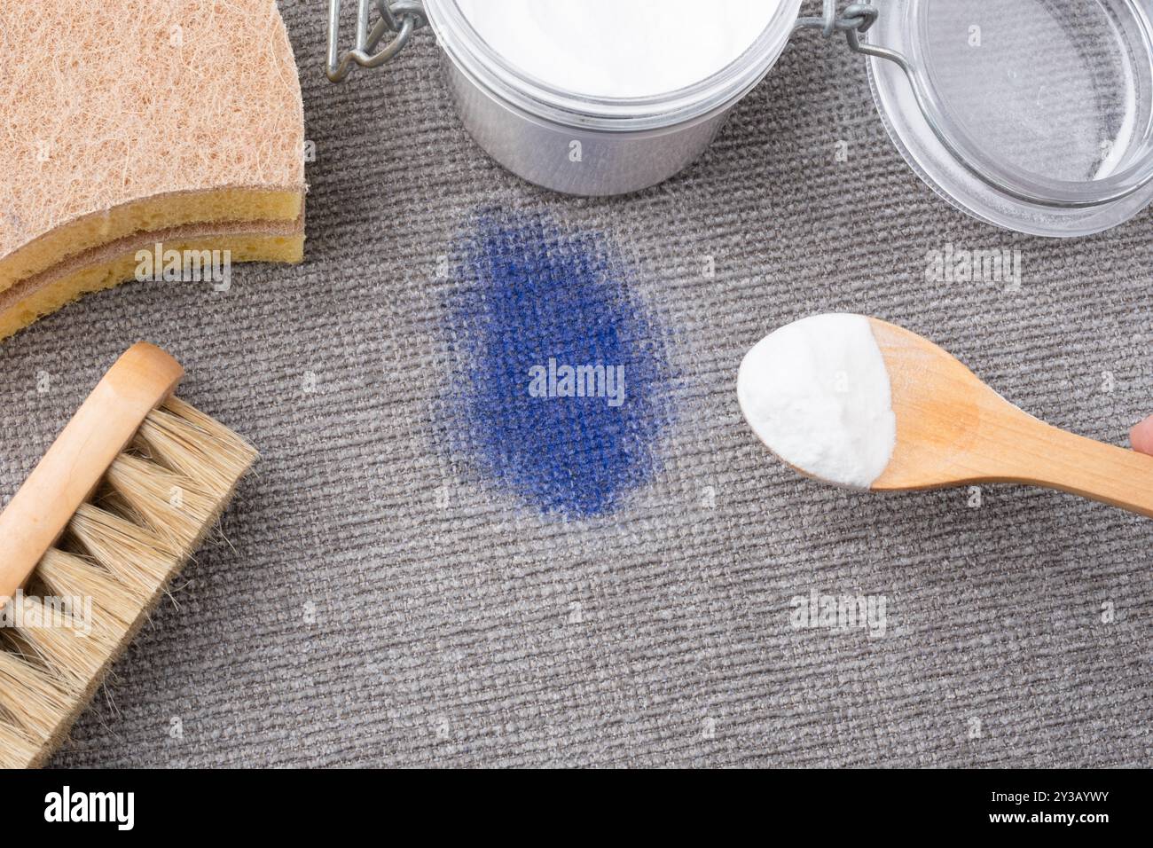 Une main de femme utilisant des ingrédients naturels bicarbonate de soude pour enlever les taches d'encre sur la sellerie texturée grise d'un canapé ou d'un tapis. vue de dessus. Phot de haute qualité Banque D'Images