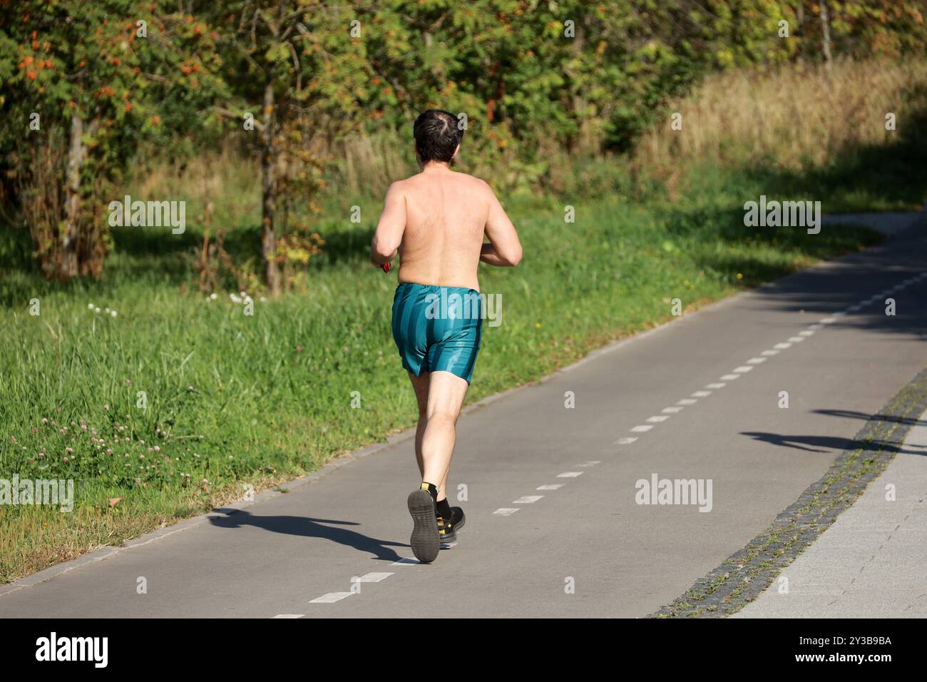 Homme en short courant sur le trottoir le long de la rue de la ville, vue arrière. Coureur dans le parc, entraînement en automne Banque D'Images