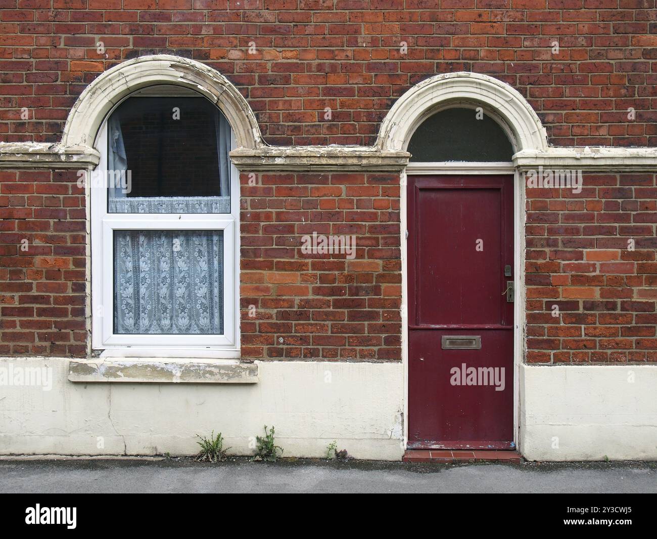 Porte d'entrée rouge et fenêtre d'une vieille maison mitoyenne britannique typique en brique avec peinture écaillée minable Banque D'Images