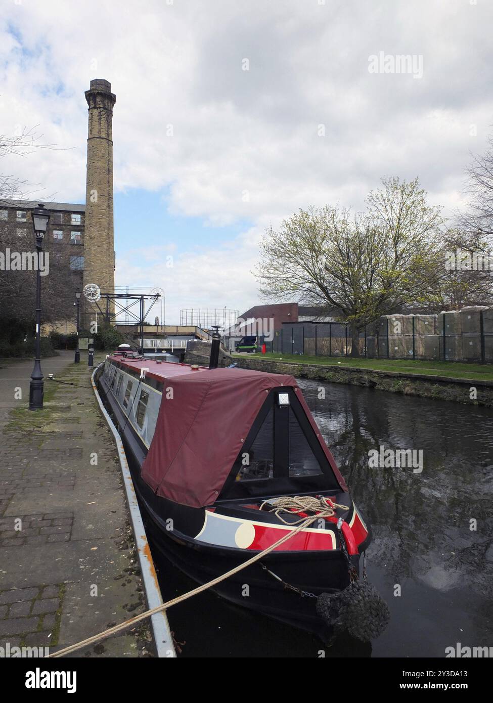 Une péniche rouge amarrée sur le canal dans le yorkshire de Huddersfield le long du chemin de remorquage avec moulin et pont en arrière-plan Banque D'Images