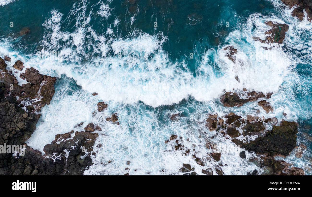 Vue aérienne des vagues de l'océan qui s'écrasent contre les rochers côtiers accidentés, montrant la beauté dynamique de l'écume marine turbulente et du littoral rocheux. Banque D'Images