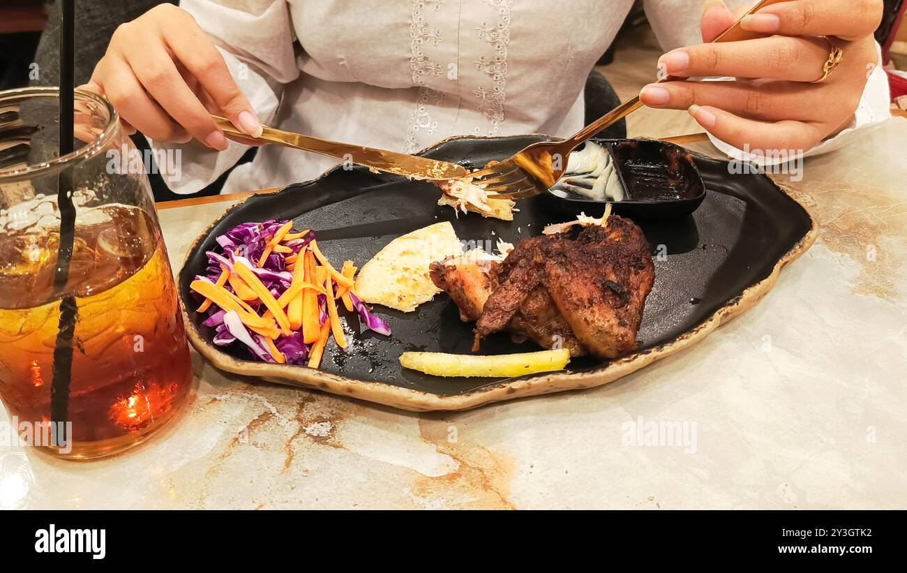 Portrait de mains de femme collectant des khubus (pain pita) accompagné de poulet rôti au four, nourriture arabe typique avec une fourchette et un couteau sur une assiette à Banque D'Images