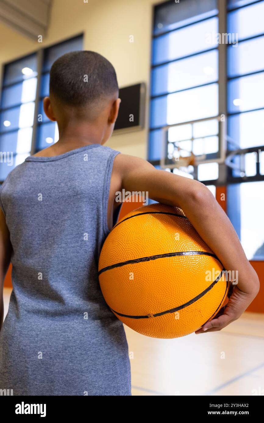 Dans le gymnase de l'école, garçon tenant le basket, regardant le cerceau, se préparant à jouer Banque D'Images