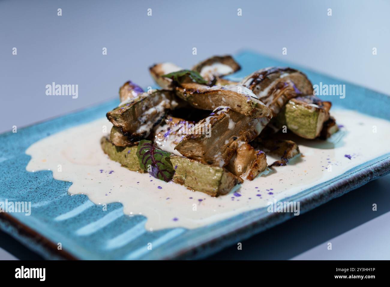 Présentation gourmande d'aubergines grillées avec filet crémeux sur une élégante assiette bleue. Banque D'Images