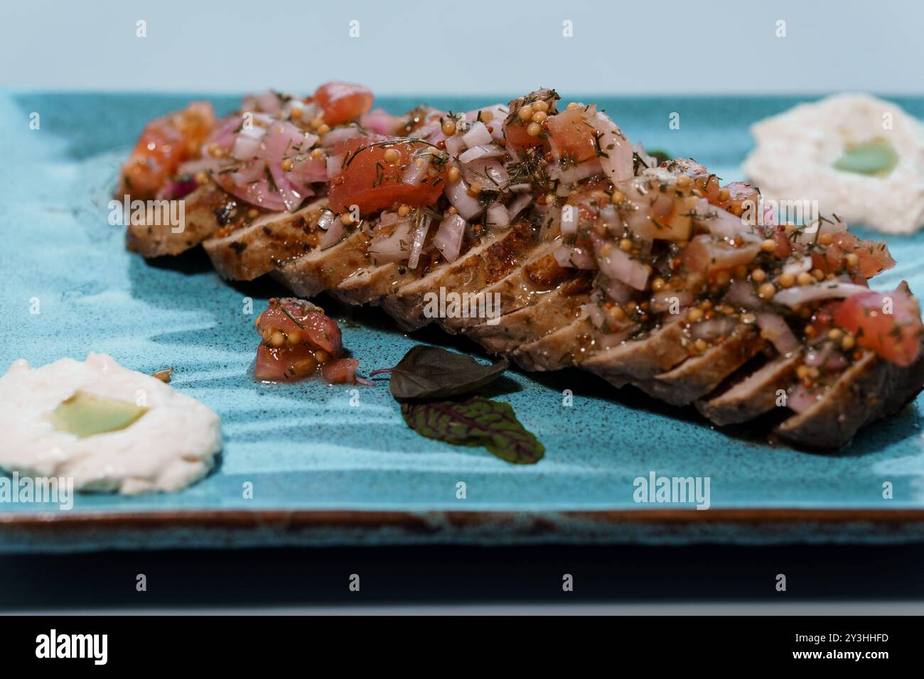 Présentation gourmande de steak grillé en tranches avec salsa fraîche sur une élégante assiette bleue. Banque D'Images
