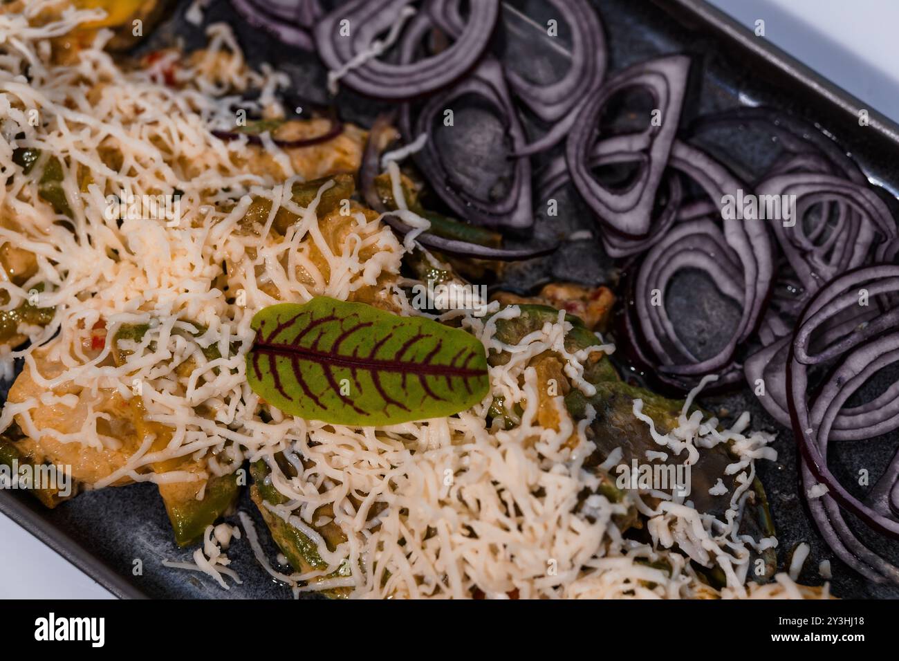 Présentation gastronomique de fromage râpé sur des légumes tranchés avec garniture élégante sur un plateau gris ardoise. Banque D'Images