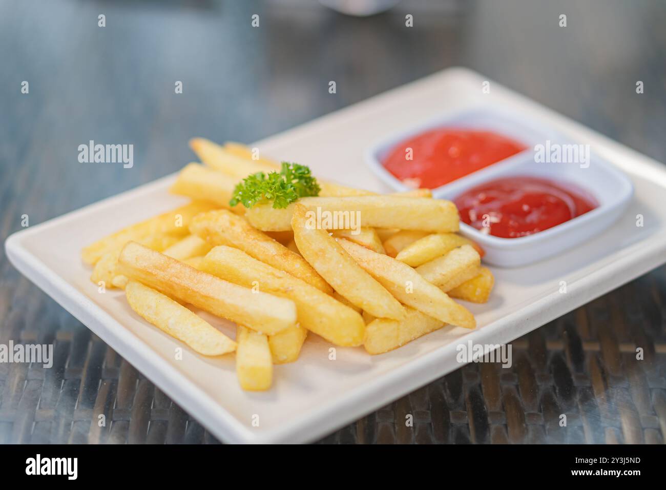 Une assiette de frites dorées servies avec deux petits bols de ketchup, garnis d'un brin de persil. Banque D'Images