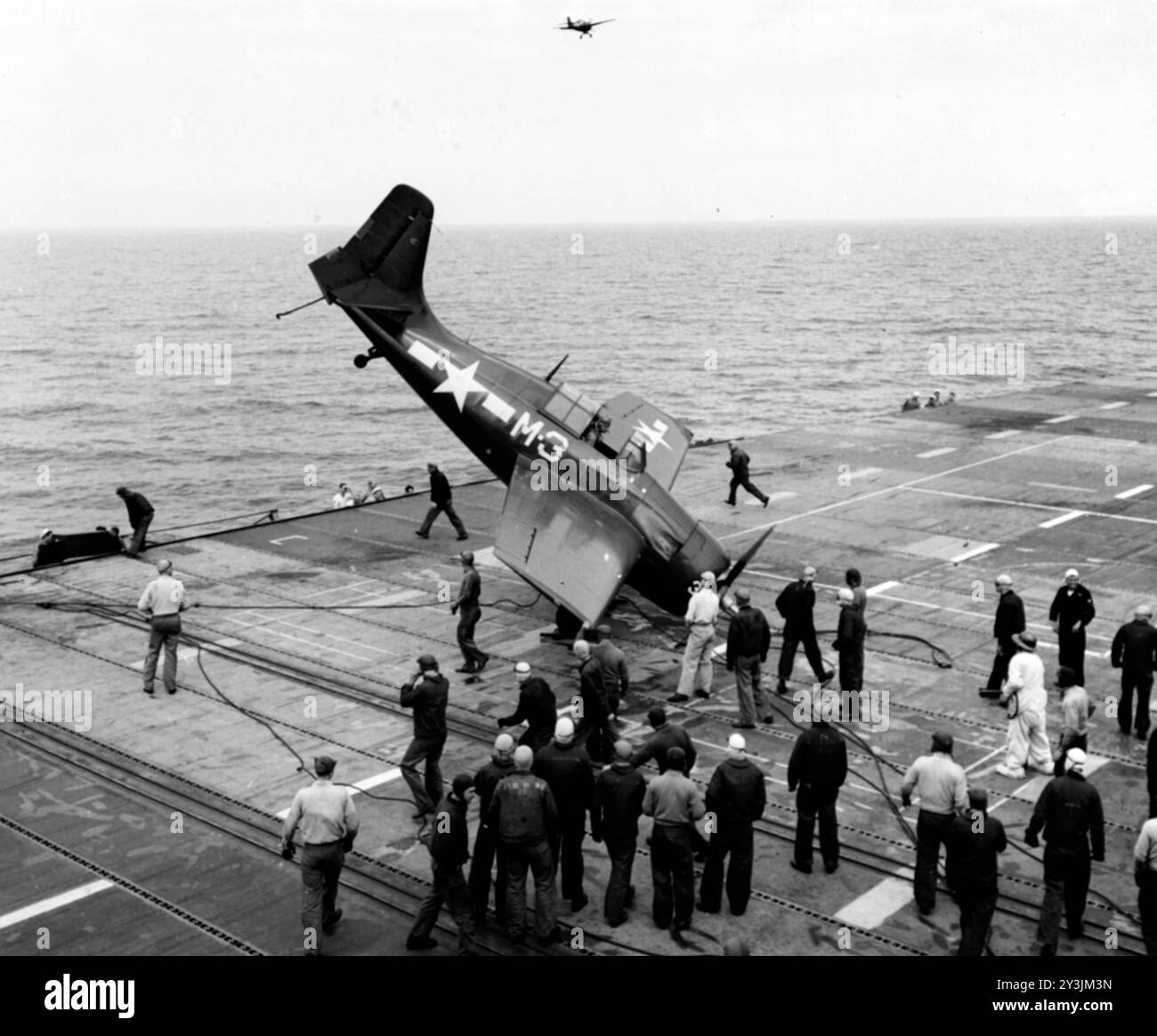 Un chasseur General Motors FM-2 Wildcat de l'US Navy a bouleversé après un écrasement de barrière à bord du porte-avions USS sable (IX-81), lors de l'entraînement des pilotes dans les grands Lacs, en mai 1945. Un autre FM-2 survole en haut au centre - photo de l'US Navy Banque D'Images