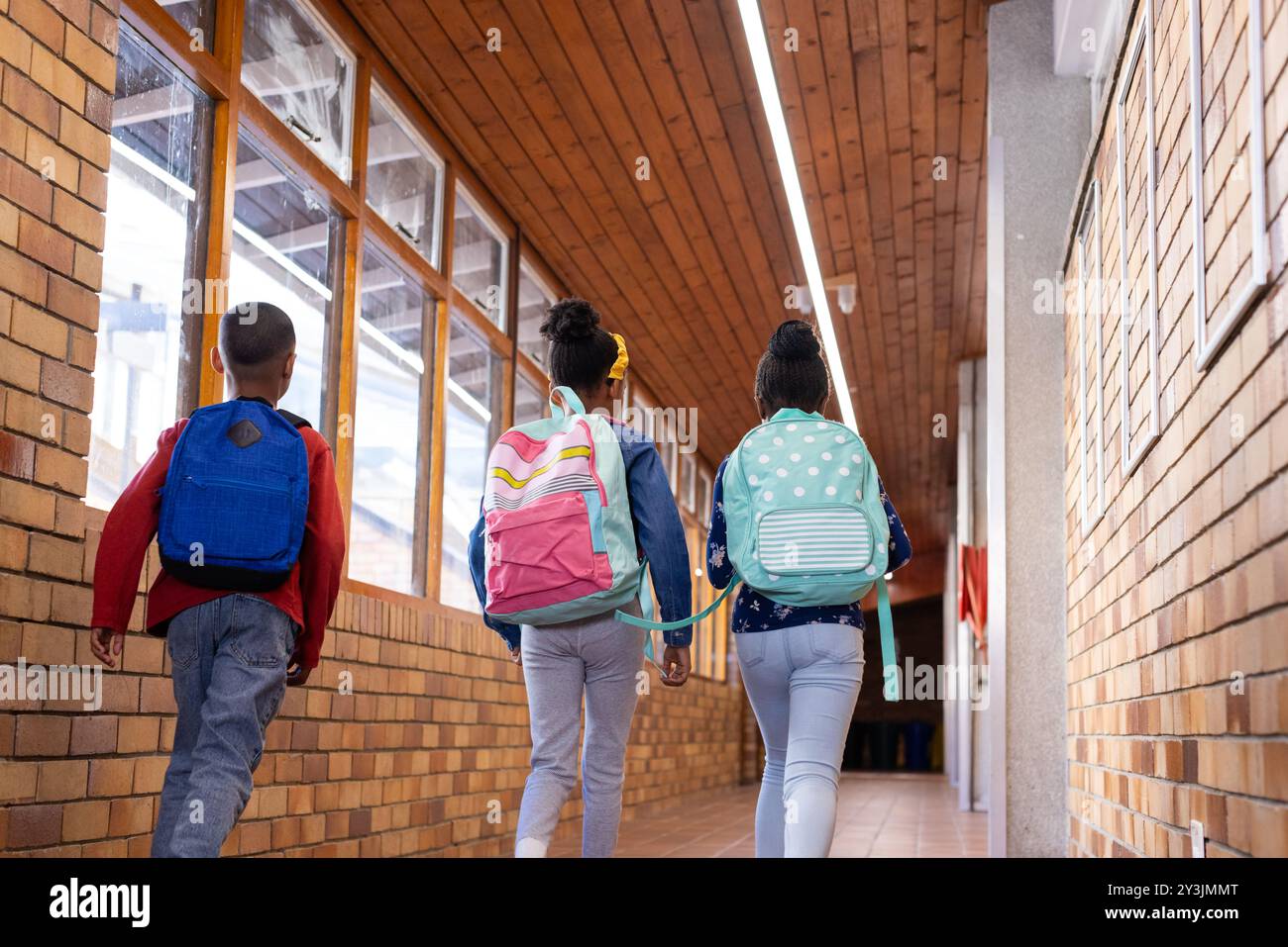 Marchant dans le couloir de l'école, deux filles multiraciales et un garçon avec des sacs à dos allant en classe Banque D'Images