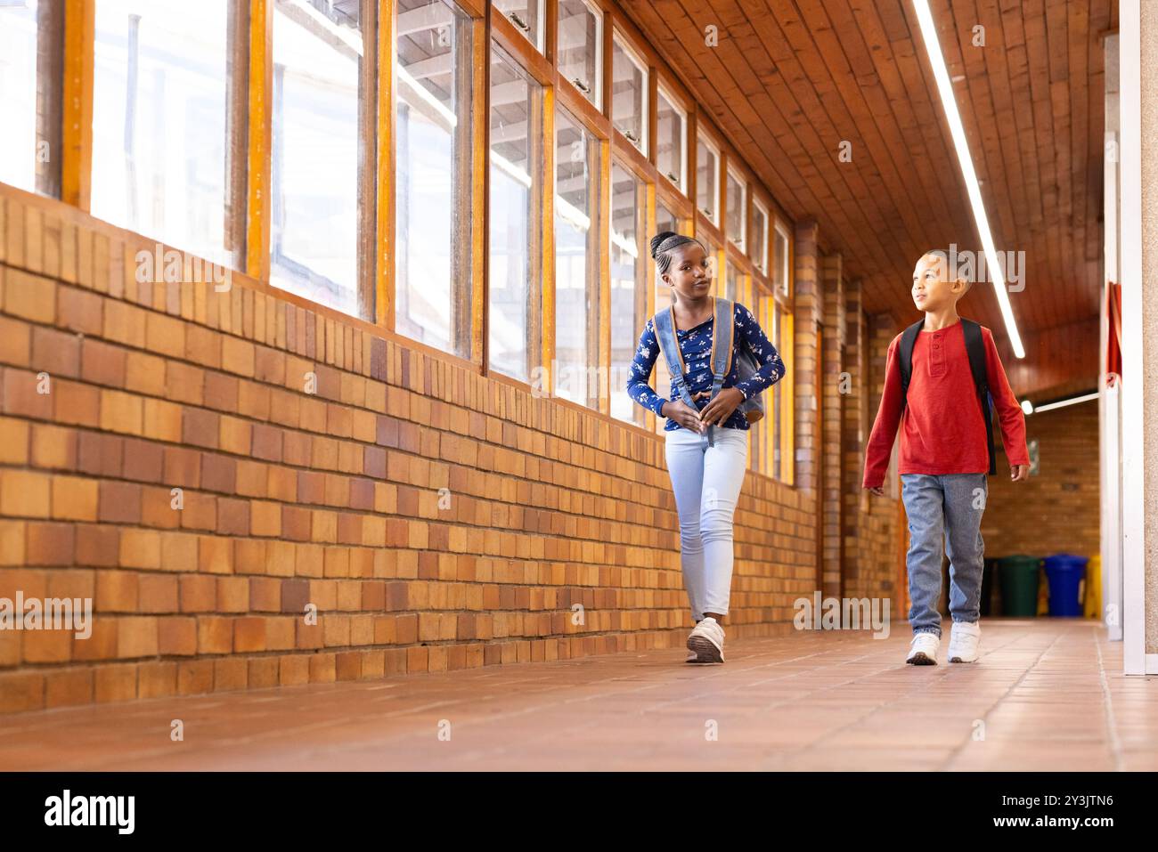 Marchant dans le couloir de l'école, deux garçons et filles multiraciaux avec des sacs à dos parlant et souriant Banque D'Images