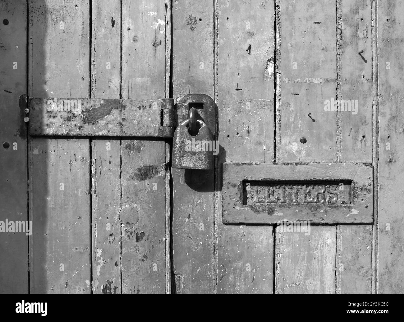 Gros plan d'une vieille porte en bois avec de la peinture décolorée fissurée et un cadenas fermé rouillé et une vieille boîte aux lettres en métal Banque D'Images