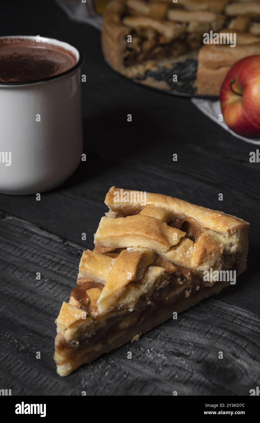 Image verticale avec une tranche de tarte aux pommes sur une table en bois rustique, une tasse de chocolat chaud et la tarte aux pommes entière. Faible luminosité. Desserts traditionnels Banque D'Images