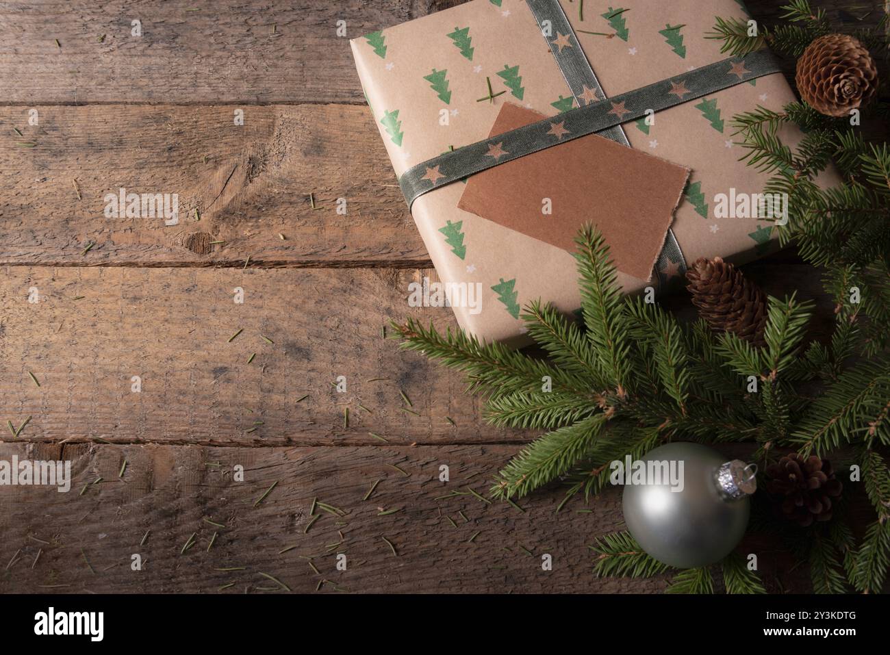 Cadre de carte de voeux de Noël avec un cadeau brun avec des arbres verts, entouré de brindilles de sapin, de pommes de pin et de boules de Noël sur une vieille table Banque D'Images