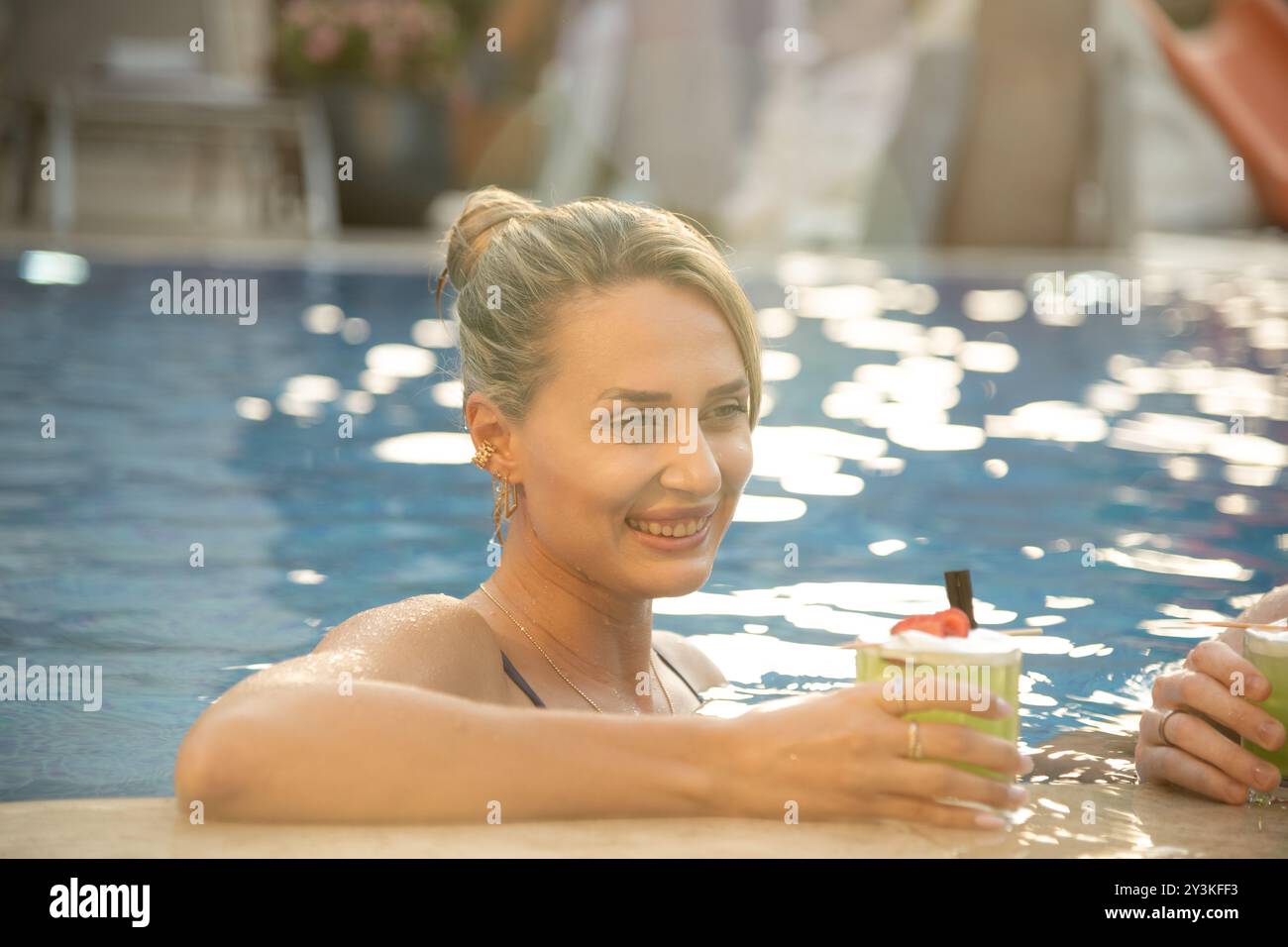 Une femme en maillot de bain entrant gracieusement dans la piscine en utilisant les escaliers, se prélasser dans l'ambiance chaleureuse de la station Banque D'Images