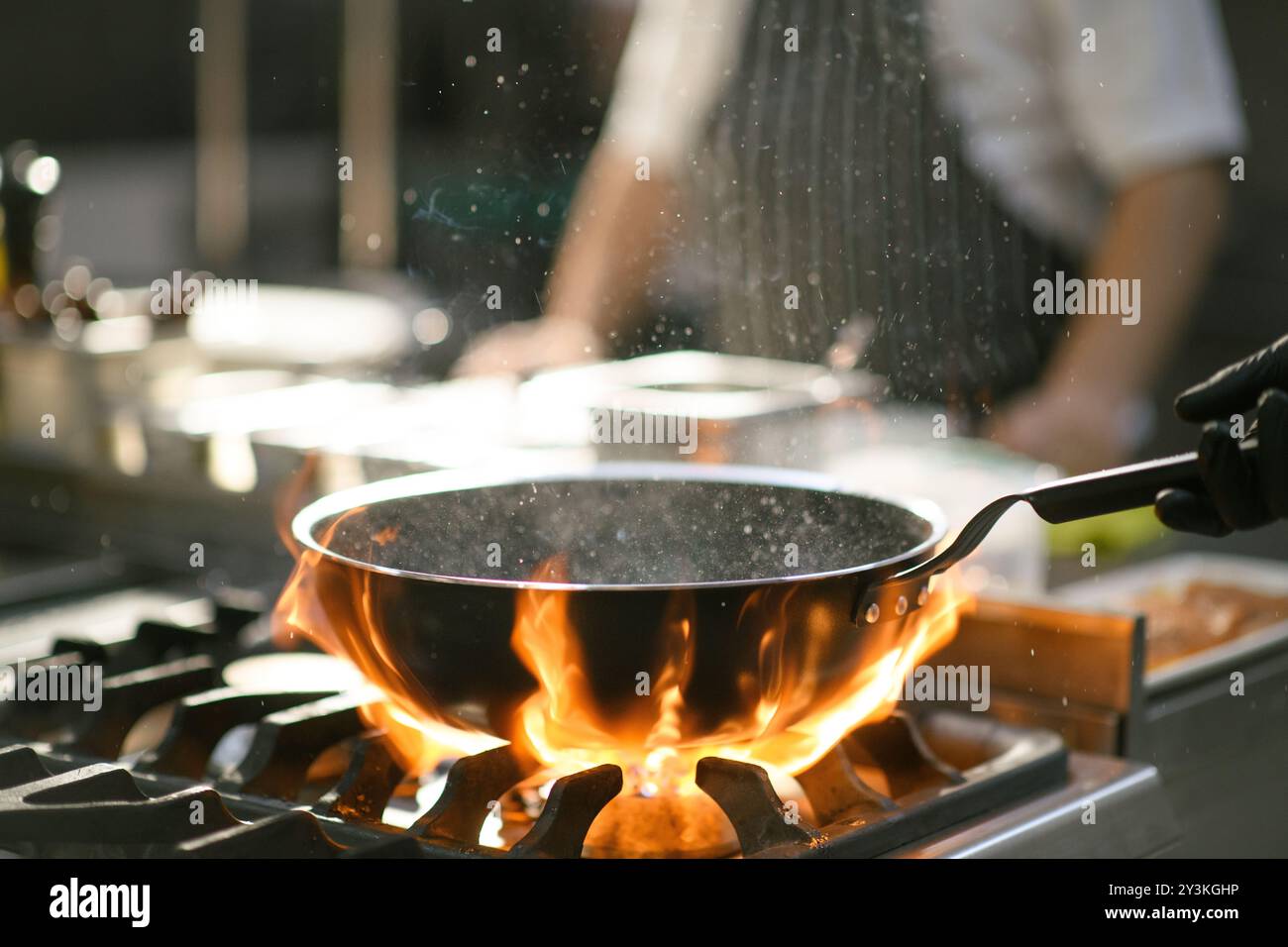 Un chef crée un éclat de flammes tout en jetant des aliments dans une casserole, affichant une technique de cuisson spectaculaire dans la cuisine de l'hôtel Banque D'Images