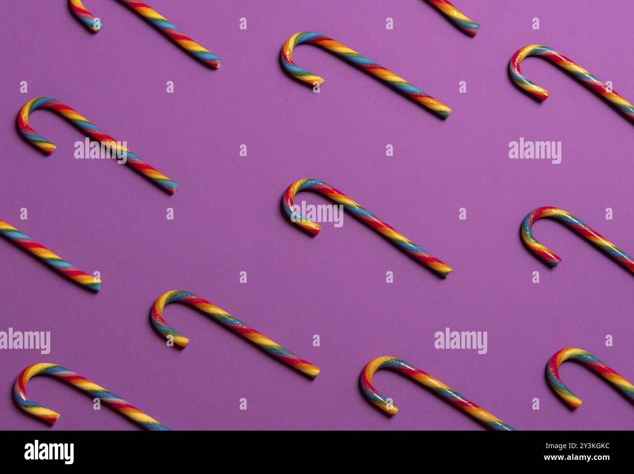 Image de Noël minimaliste avec des cannes de bonbon colorées arc-en-ciel, affichées dans un motif sur un fond de papier violet Banque D'Images