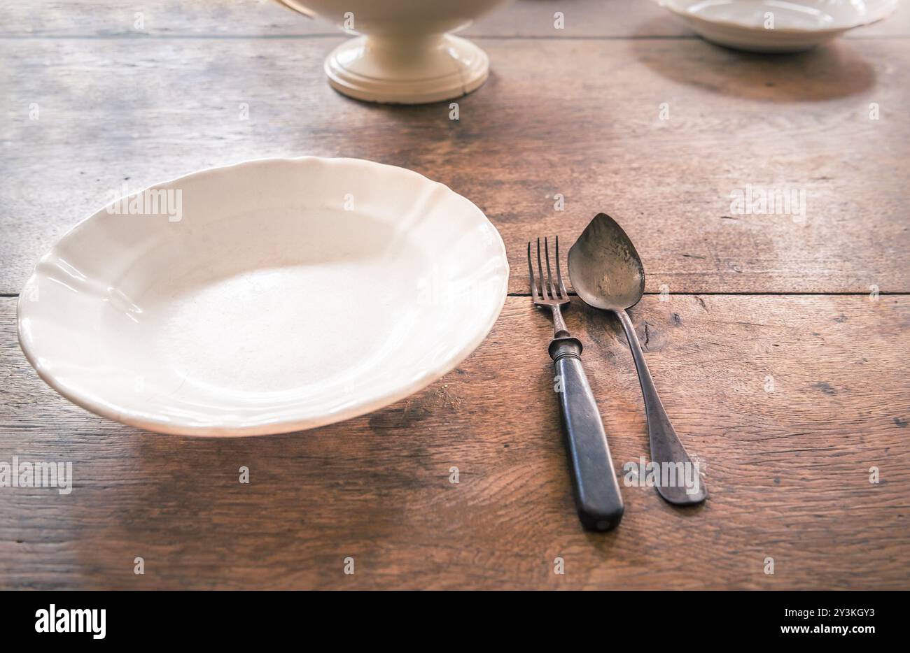 Cadre de dîner rustique avec un vieux plat blanc et fourchette et cuillère en métal altéré, placé sur une table en bois, avec d'autres vaisselle en arrière-plan Banque D'Images