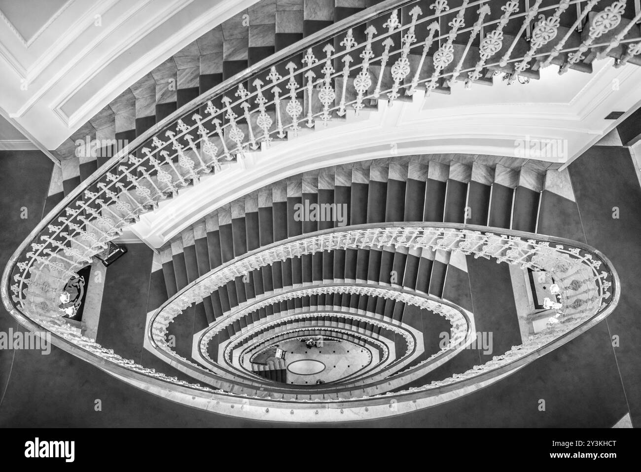 Image monochrome d'escaliers en colimaçon en marbre avec un tapis rouge et une élégante balustrade, vue d'en haut Banque D'Images