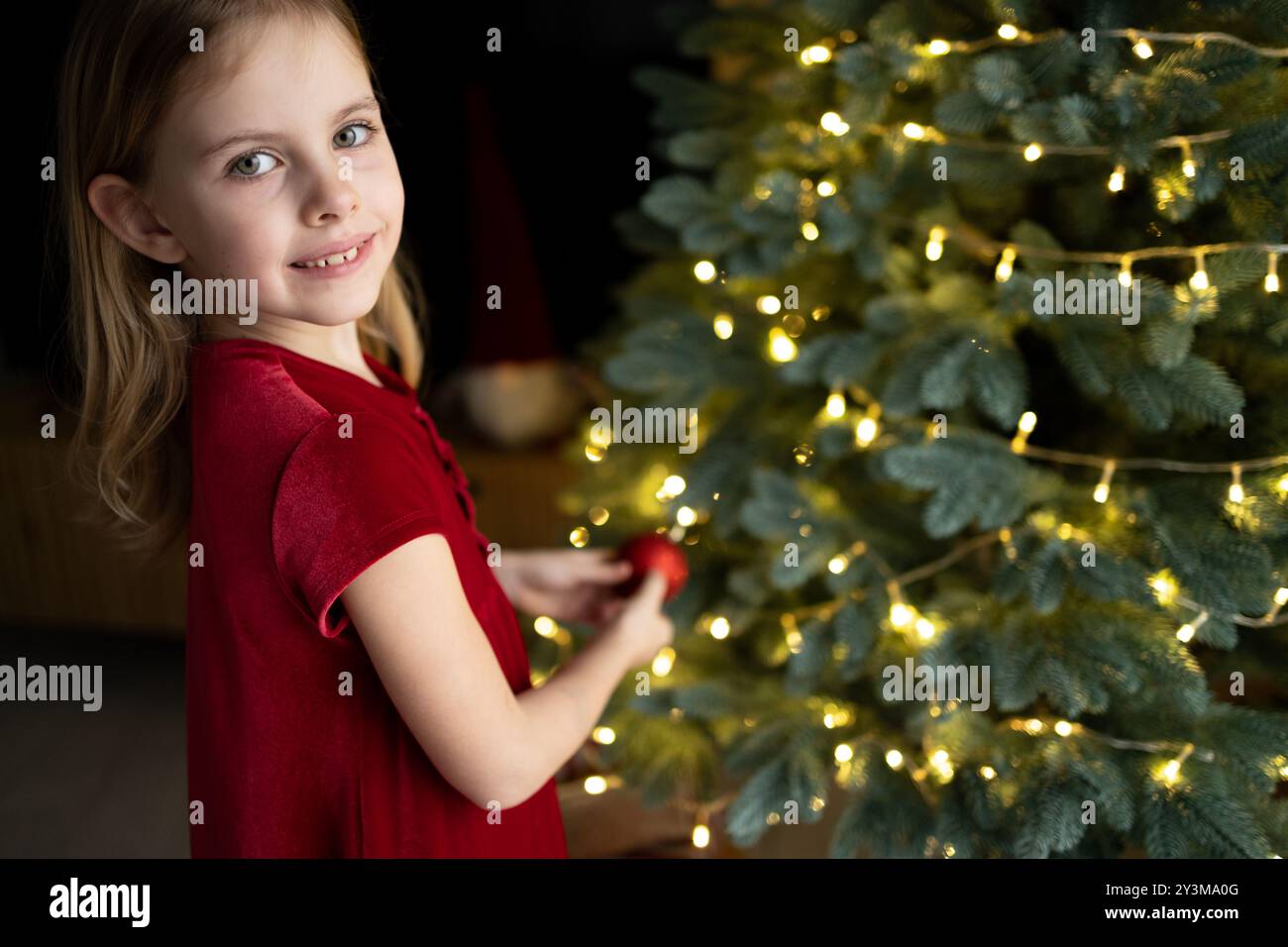 Petite fille décorant l'arbre de Noël avec des ornements et des lumières à la maison Banque D'Images