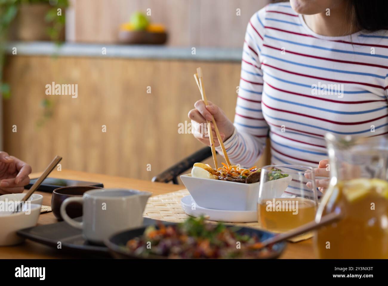 À la maison, manger de la cuisine asiatique, jeune femme utilisant des baguettes à la table à manger avec la famille Banque D'Images