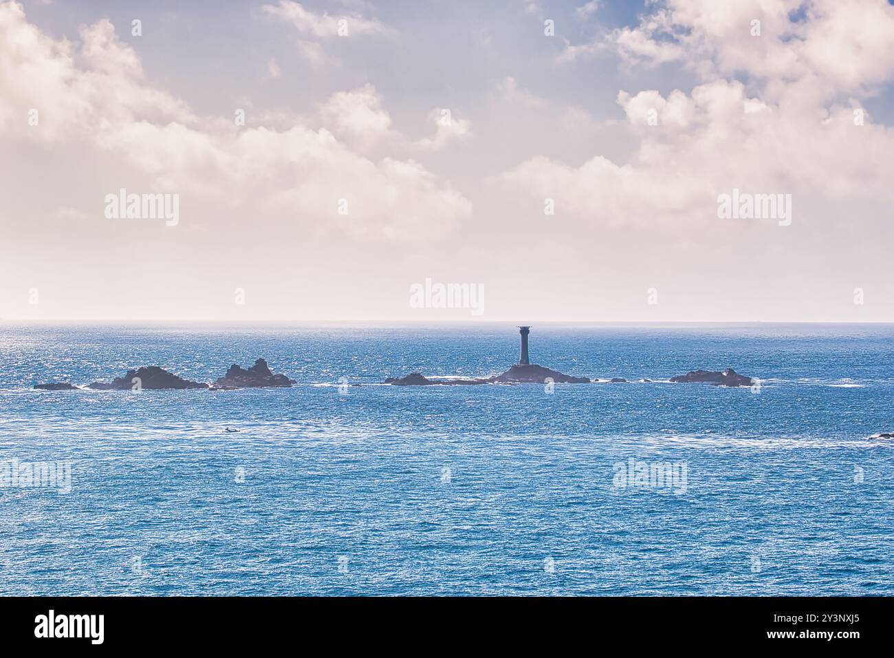 Un paysage marin serein avec un phare lointain sur une île rocheuse, entouré par des eaux bleues calmes et un ciel nuageux. Banque D'Images