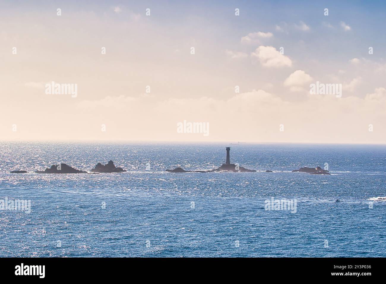 Un paysage marin tranquille avec un phare lointain sur des îlots rocheux, entouré d'eaux bleues chatoyantes sous un ciel partiellement nuageux. Banque D'Images