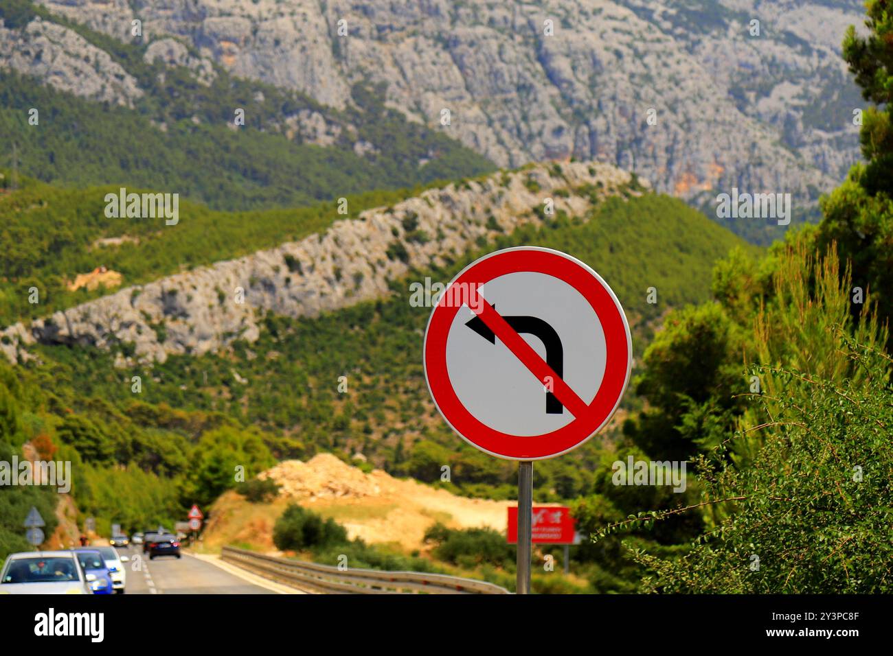 Panneau routier - tourner à gauche est interdit, flèche noire sur fond blanc, barrée en rouge. Aucun virage à gauche contre de belles montagnes. Interdiction routière Banque D'Images