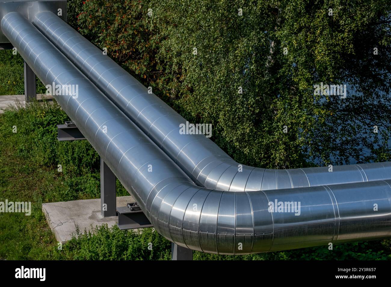 tuyaux en métal argenté arge pour le chauffage urbain avec des feuilles vertes en arrière-plan Banque D'Images