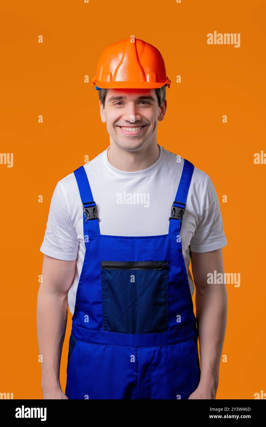 Portrait souriant sympathique de bricoleur sur studio orange. Homme de constructeur positif, casque Banque D'Images