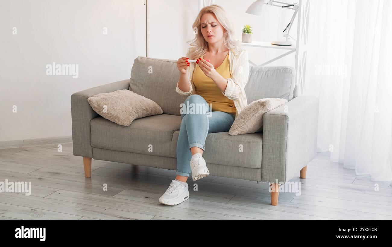 Attente de maternité. Femme inquiète. Nouvelles inattendues. Dame sérieuse obtenant un résultat de test négatif assis canapé intérieur de la salle de lumière. Banque D'Images