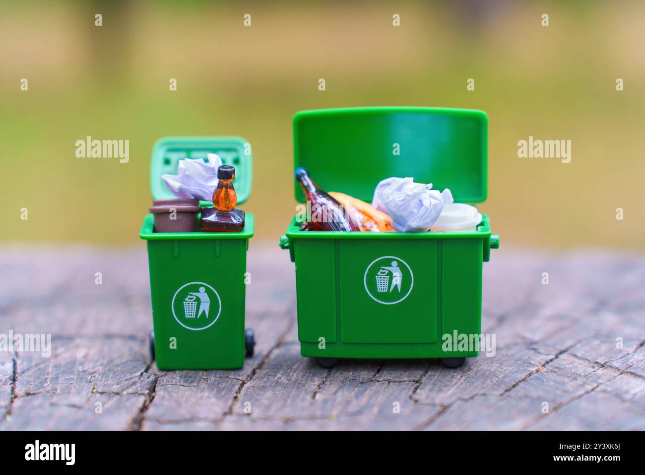Deux poubelles miniatures vertes remplies de déchets assortis sur une surface en bois, présentant des concepts de recyclage et de gestion des déchets. Banque D'Images