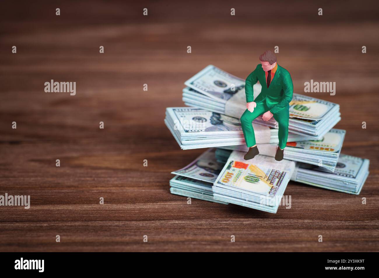 Figure d'homme d'affaires assis sur des piles d'argent liquide sur la surface en bois, représentant la richesse, l'analyse financière, et les décisions d'investissement. Banque D'Images