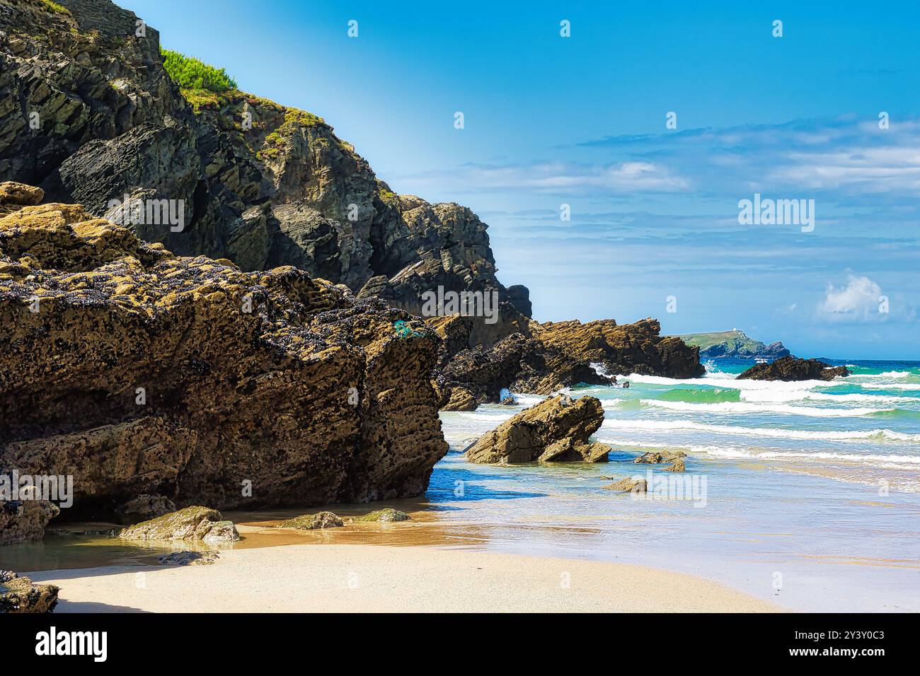 Une plage pittoresque avec des falaises escarpées et des formations rocheuses le long du rivage. Les vagues se jettent doucement sur la plage de sable sous un blu lumineux Banque D'Images