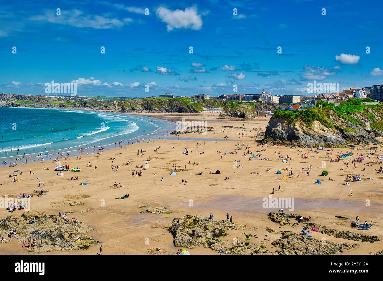 Une scène de plage dynamique avec de nombreuses personnes profitant du soleil et du sable. Le littoral présente des falaises rocheuses et de douces vagues qui se détendent sur le rivage. Le s Banque D'Images