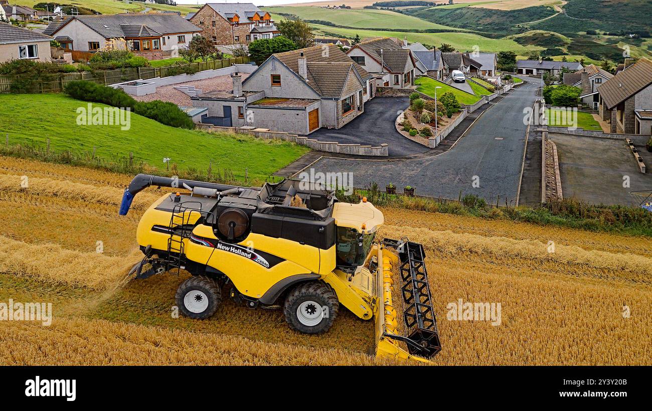 Combinez Harvester Gardenstown Aberdeenshire Scotland quelques maisons de village et une moissonneuse dans le champ à la fin de l'été Banque D'Images