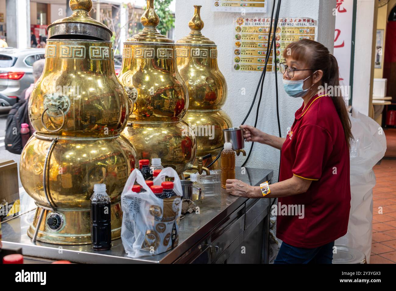 Un assistant préparant et remplissant du thé chinois fraîchement préparé dans un ensemble de distributeurs de thé chinois traditionnels en laiton pour les clients de passage dans Smith S. Banque D'Images