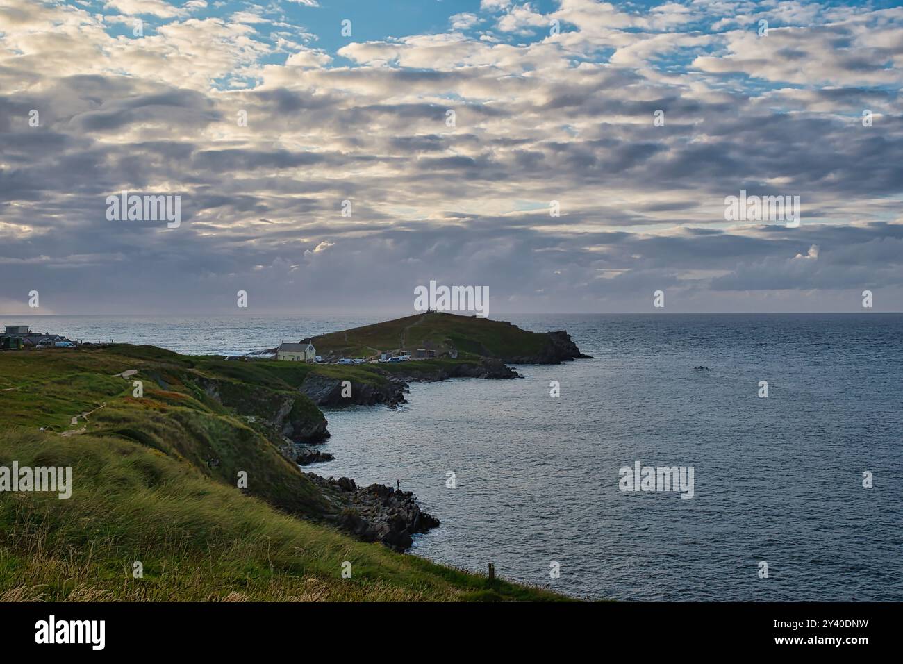 Une vue panoramique sur la côte avec une colline herbeuse menant à l'océan. Au loin, une petite île est visible avec un phare au sommet, UEDN Banque D'Images