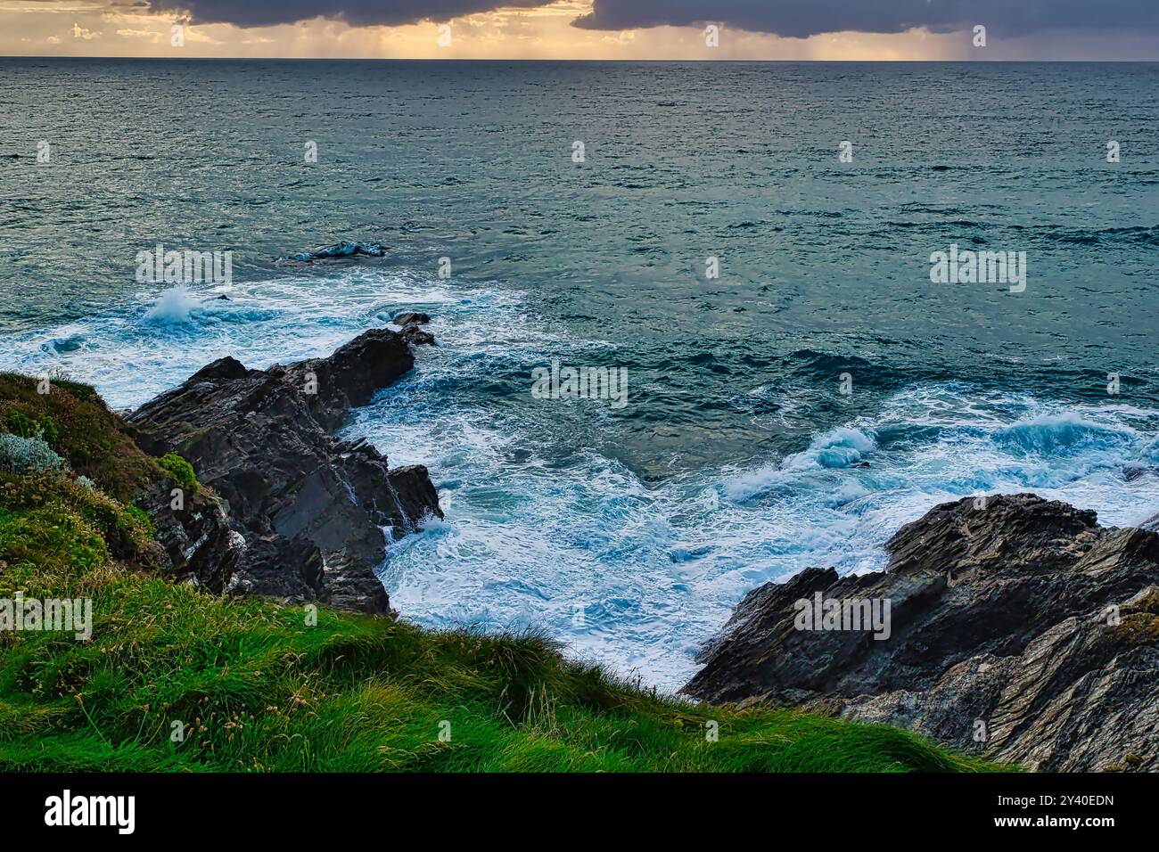 Une vue panoramique sur l'océan avec des falaises rocheuses et des vagues qui s'écrasent contre eux. Le ciel est partiellement nuageux avec un soupçon de lumière du soleil jetant un coup d'œil à travers le CLO Banque D'Images