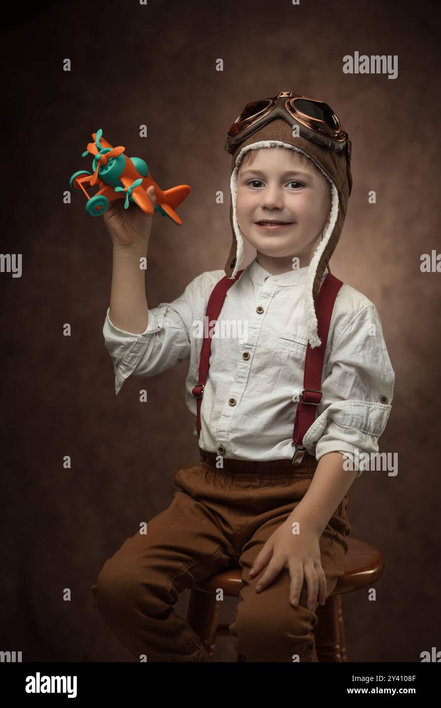 Pilote enfant avec casquette aviateur et avion jouet, portrait rétro d'un garçon vêtu de vêtements vintage sur fond marron vieux Banque D'Images
