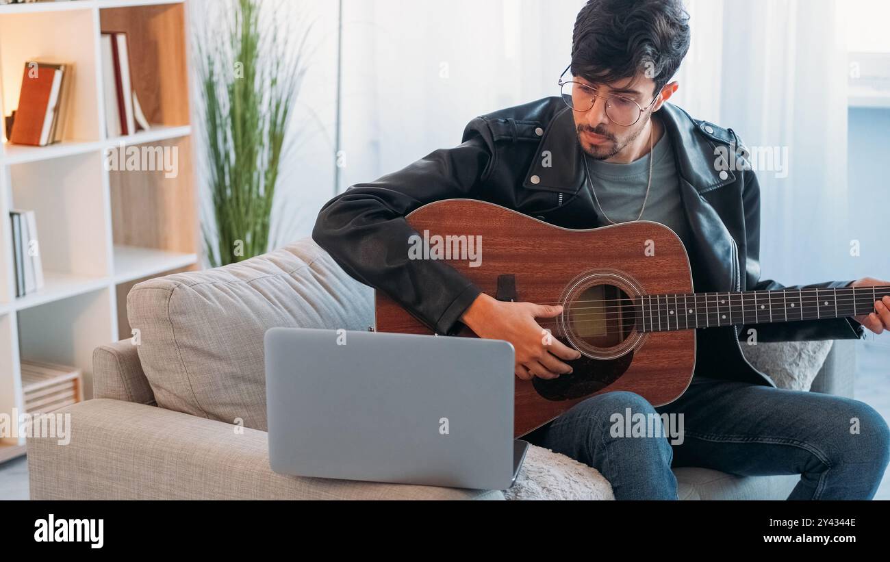 Cours de guitare en ligne. Cours de musique. Passe-temps créatif. Musicien talentueux apprenant à jouer un instrument acoustique regardant une leçon vidéo sur ordinateur portable à l'intérieur de la maison avec de l'espace libre. Banque D'Images