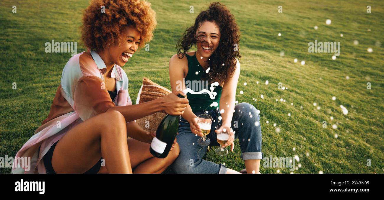 Joyeux étudiants universitaires célèbrent la fin de leur période d'examen, partageant rire, champagne et bonheur dans un cadre de jardin pittoresque Banque D'Images