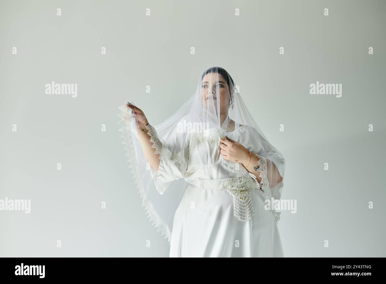 Une superbe jeune femme dans une robe blanche et des boucles d'oreilles pose gracieusement, mettant en valeur son élégance nuptiale. Banque D'Images