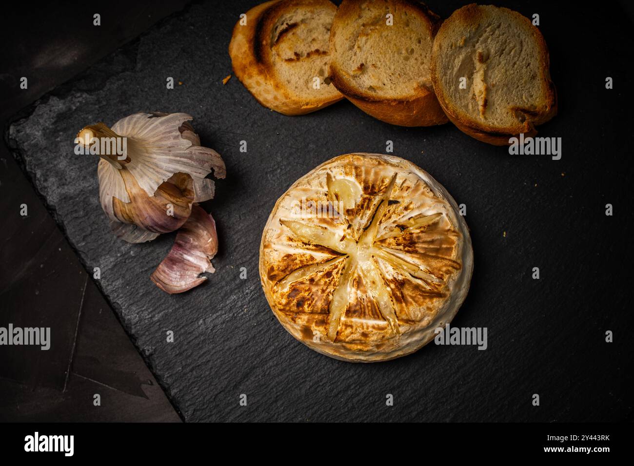 Brie ou camembert cuit au four sur fond noir avec du pain grillé ou des toasts et de l'ail. Photo de haute qualité Banque D'Images
