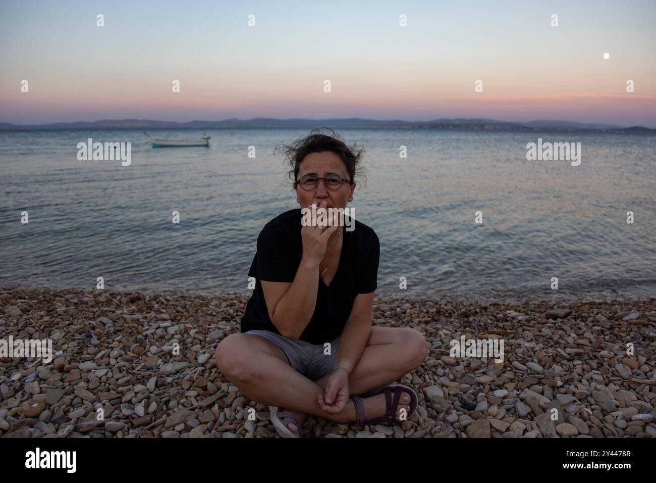 Femme mature avec des lunettes fumant sur la plage au coucher du soleil Banque D'Images