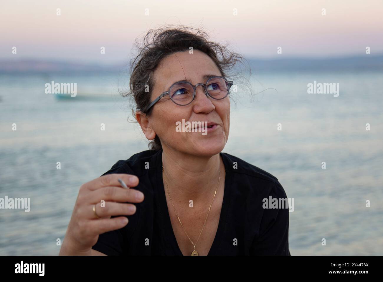 Femme mature avec des lunettes fumant sur la plage au coucher du soleil Banque D'Images