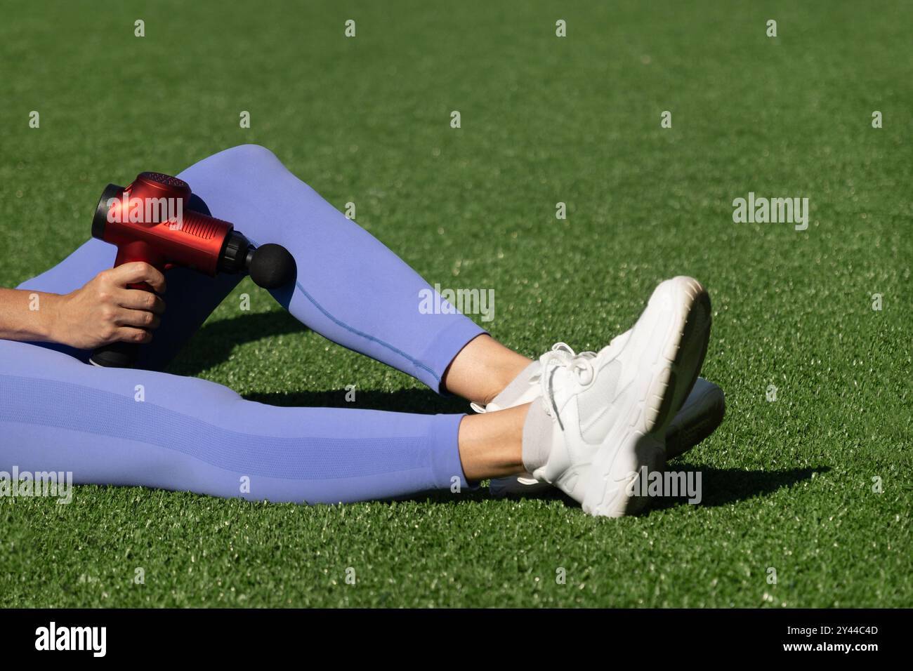 Femme massant les jambes avec le pistolet à percussion de massage après l'entraînement. Pistolet masseur à percussion thérapeutique. Banque D'Images